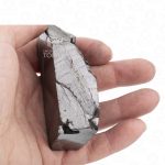 Authentic noble shungite raw stone held in hand for scale. Mined exclusively in the Shunga region of Karelia — the world’s only source of this mineral.