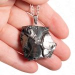 Square-shaped black mineral pendant on steel chain resting in a hand